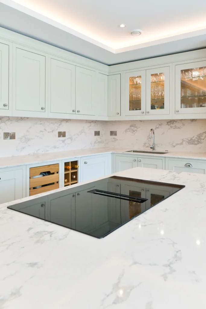 Pale cream shaker cabinets featuring glass display doors and integrated warm internal lighting over a sink