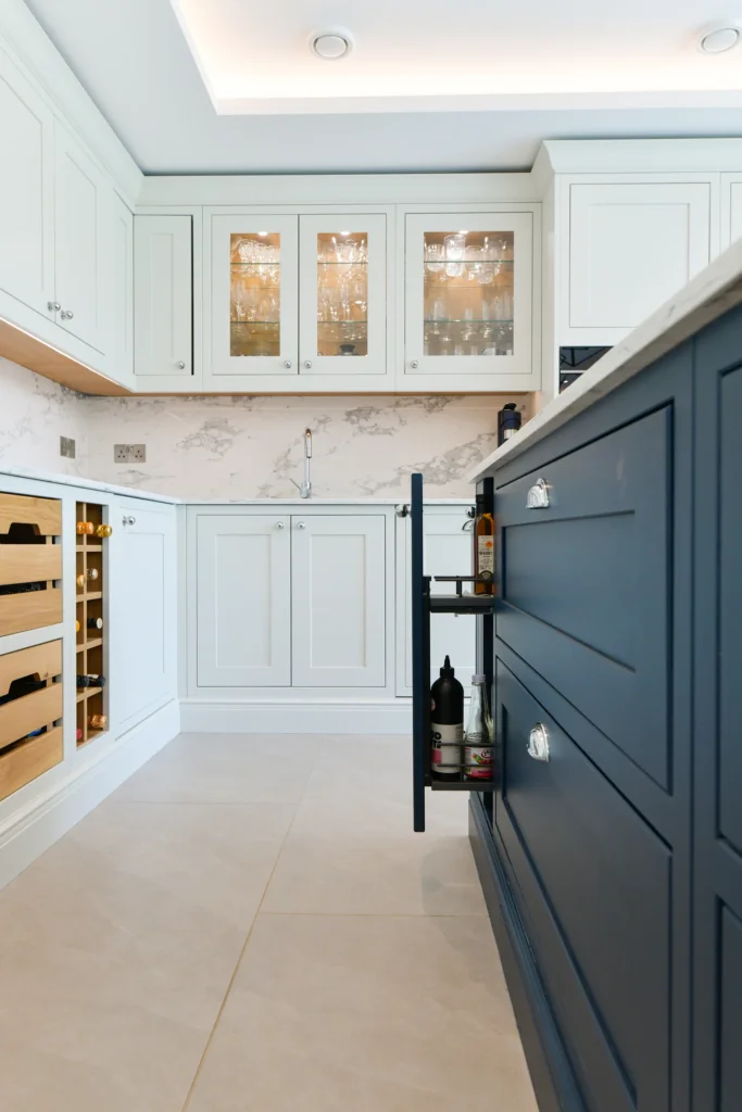 Pale cream shaker cabinets featuring glass display doors and integrated warm internal lighting over a sink